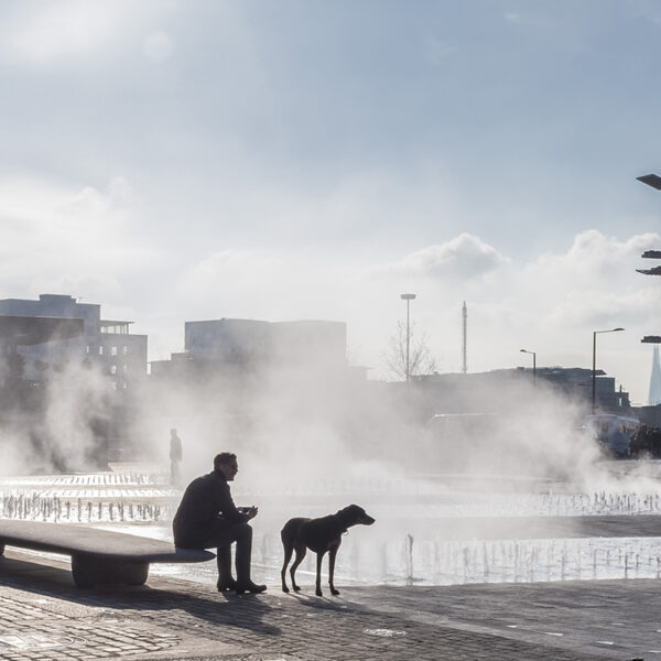 A man and his dog enjoy the morning mist from Granary Square fountains
